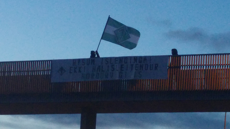 Nordic Resistance Movement members in Iceland hold a banner and flag on a bridge