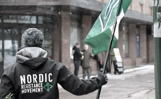 A Nordic Resistance Movement member holds a Tyr Rune flag in Horten, Norway