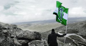 Man holds a Nordic Resistance Movement flag in the mountains