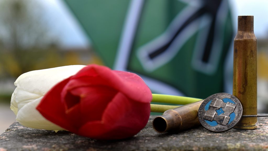 Flowers, a pin badge and bullet cartridges in front of the Nordic Resistance Movement flag